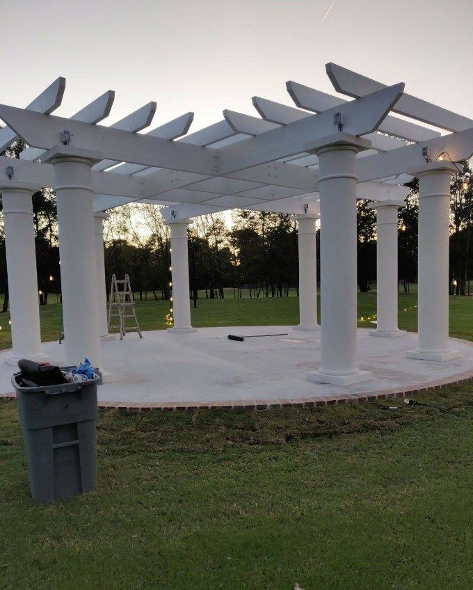 A pergola is being built in a park with a trash can in front of it.
