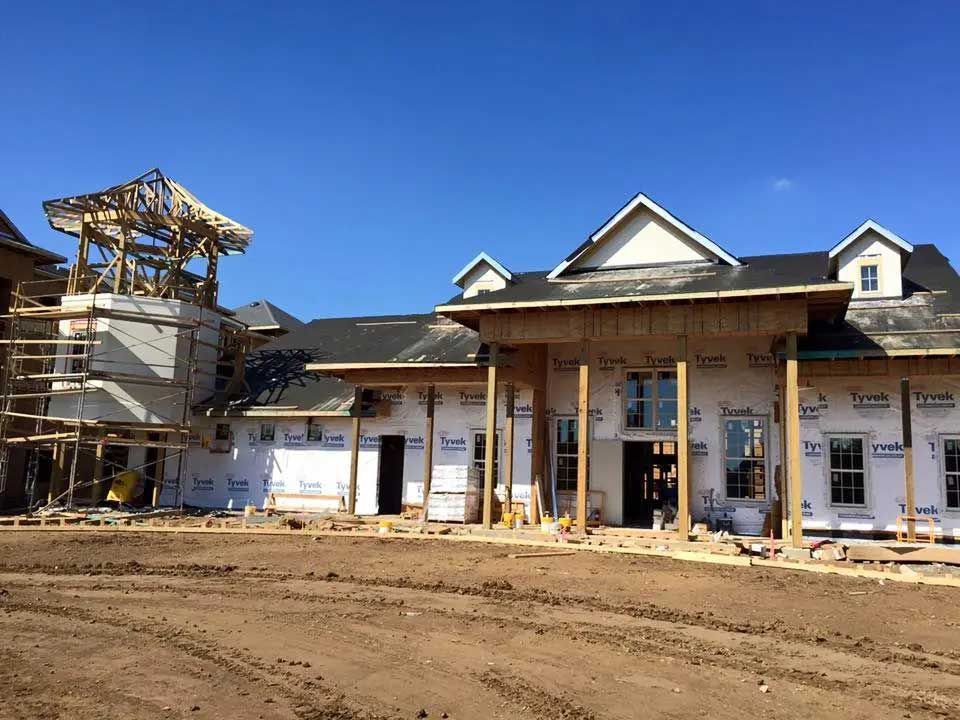 A large house is being built in the middle of a dirt field.