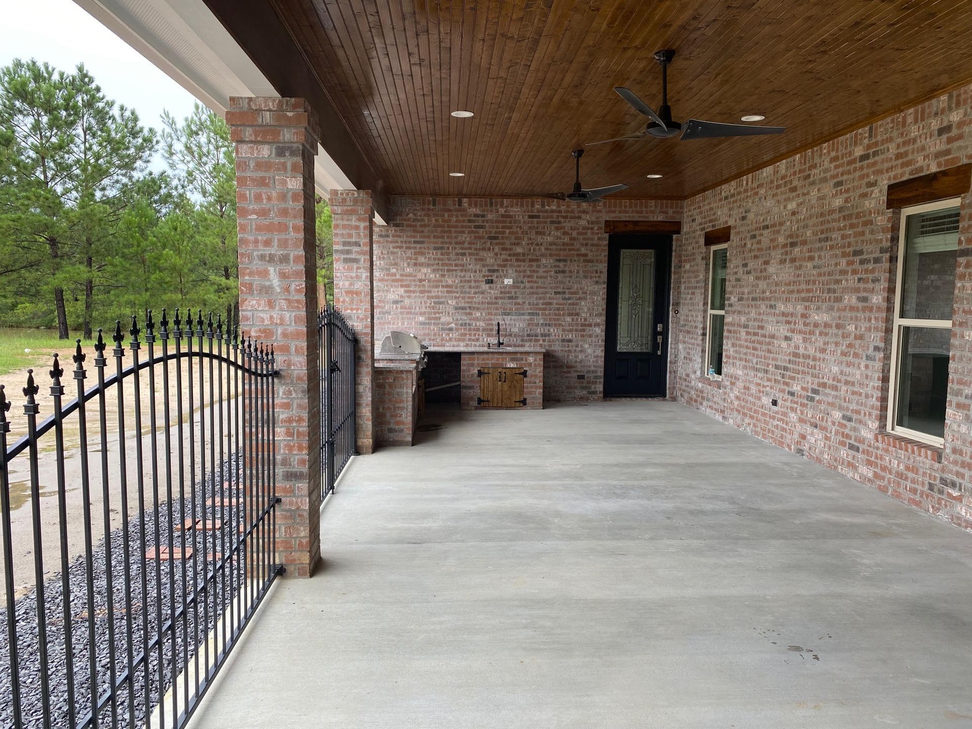 Covered patio with brick walls, concrete floor, wrought iron fence, and black door.