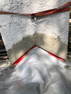 A chimney base shows fresh, light-colored mortar patching along red metal flashing, with a white protective sheet below.