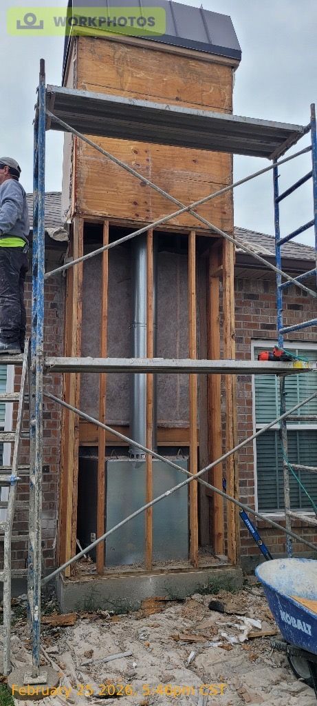 A person works on scaffolding around a partially dismantled chimney structure on the side of a brick house.