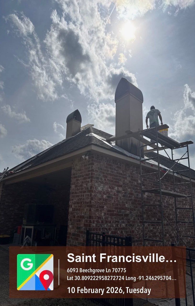 A worker on scaffolding repairs a brick chimney on a house roof under a sunny, cloudy sky in Saint Francisville.