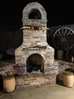 A brick outdoor fireplace decorated with a set of steer horns, a rifle, and western-themed items like barrels and a wheel.