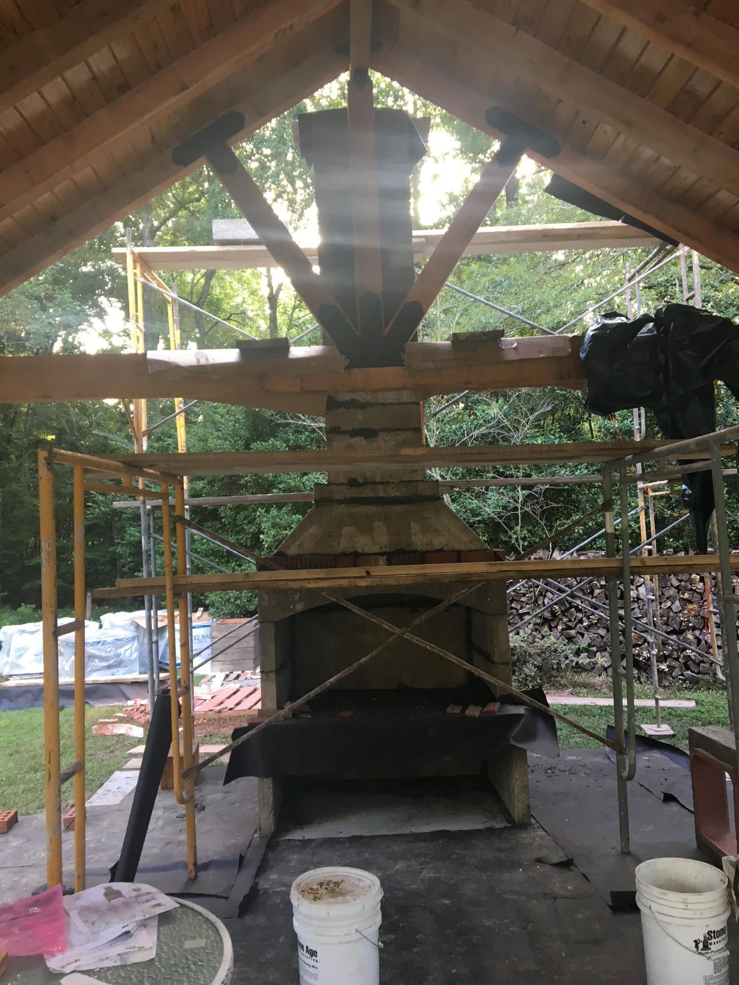 Outdoor fireplace under construction with scaffolding and wooden beams.