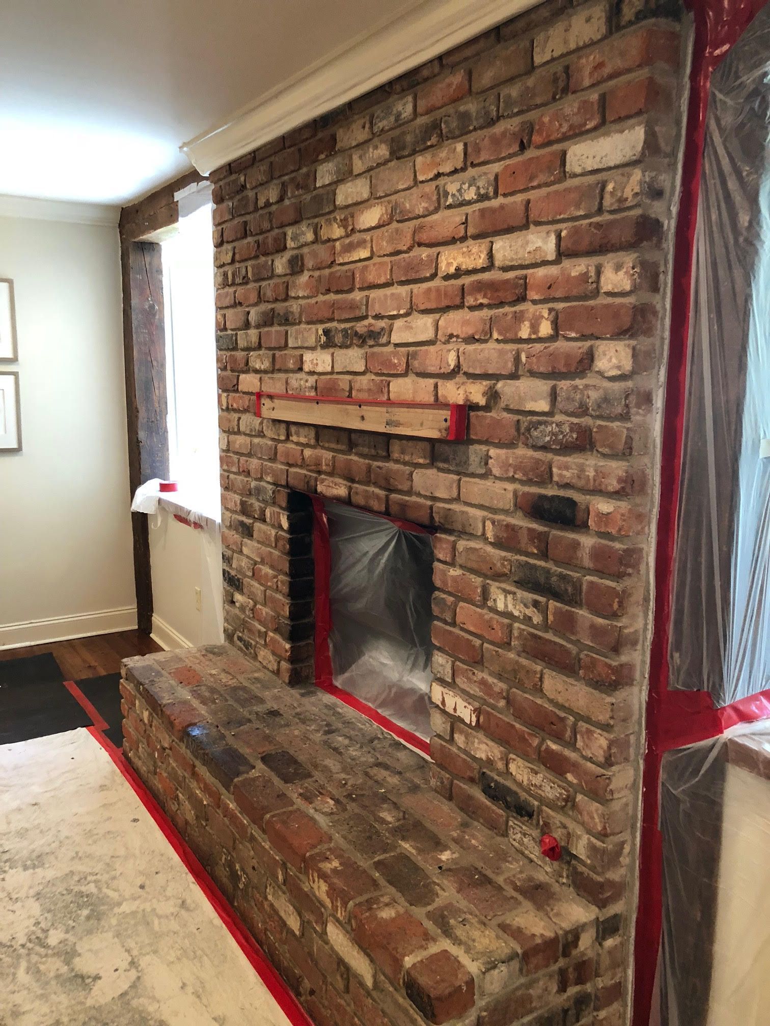 Brick fireplace with a wood mantel and hearth, protected with plastic sheeting.