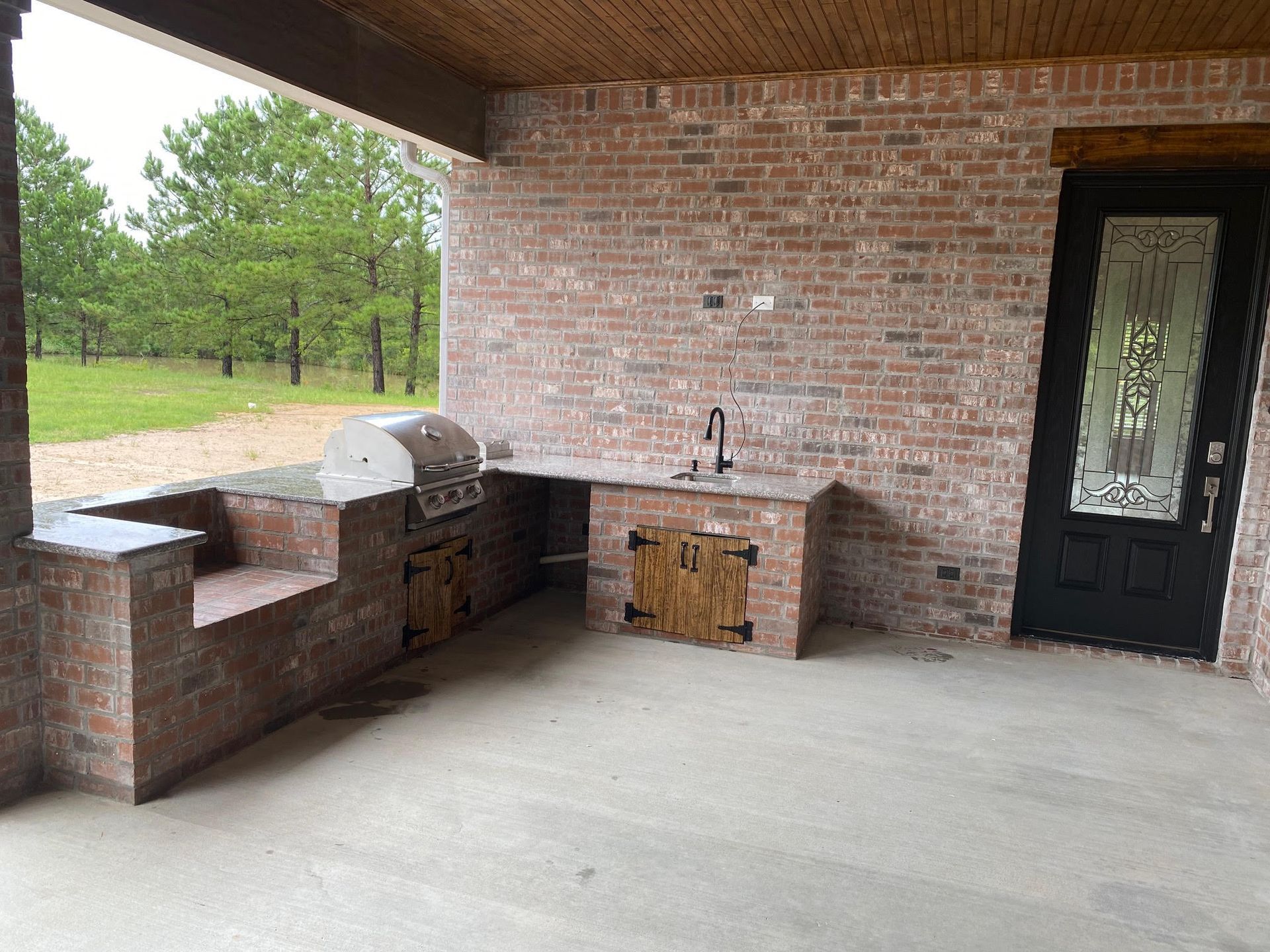 Outdoor brick kitchen with grill, sink, and cabinets under a covered patio.