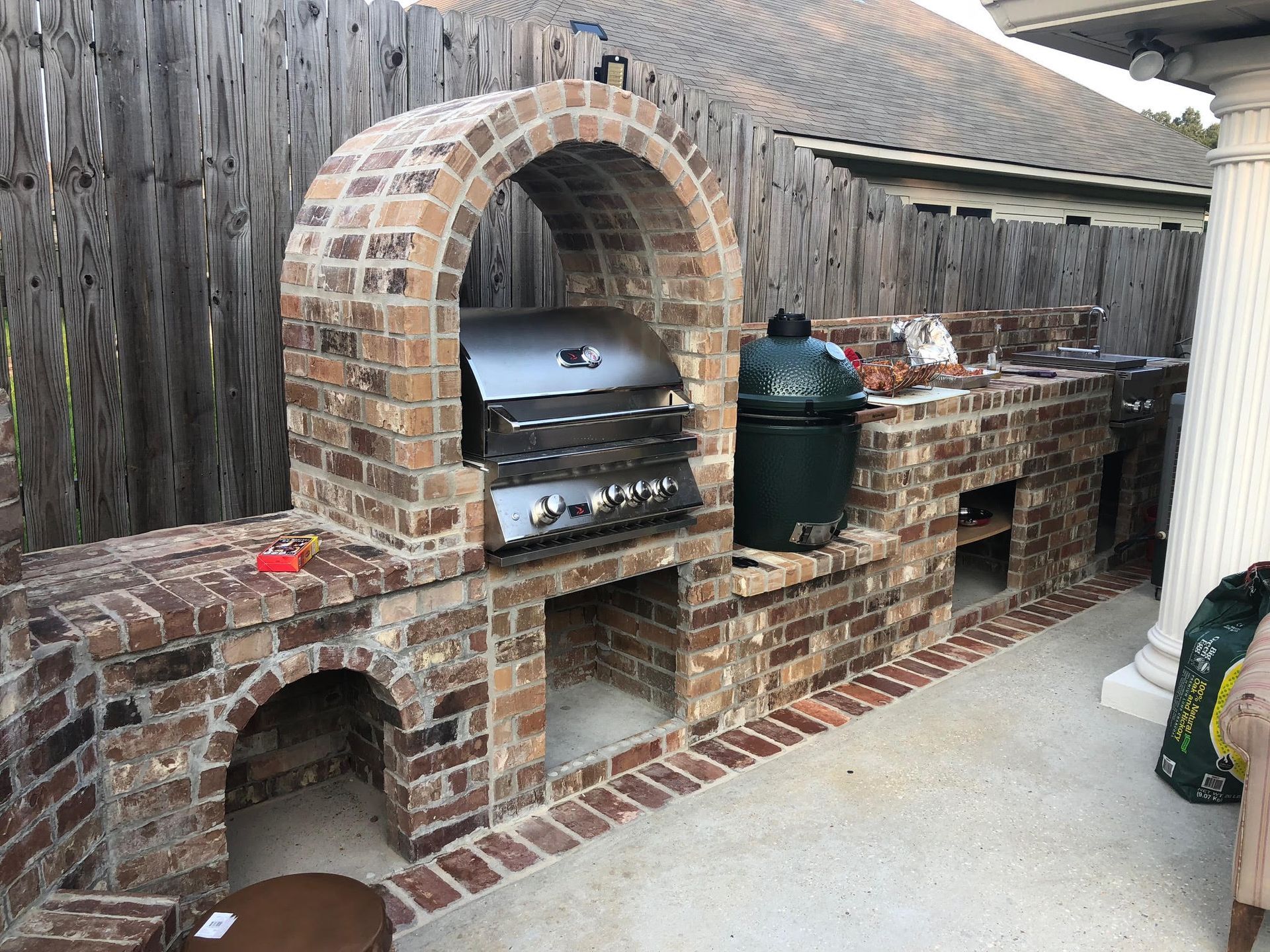 Brick outdoor kitchen with a grill, Big Green Egg, and arched structure.