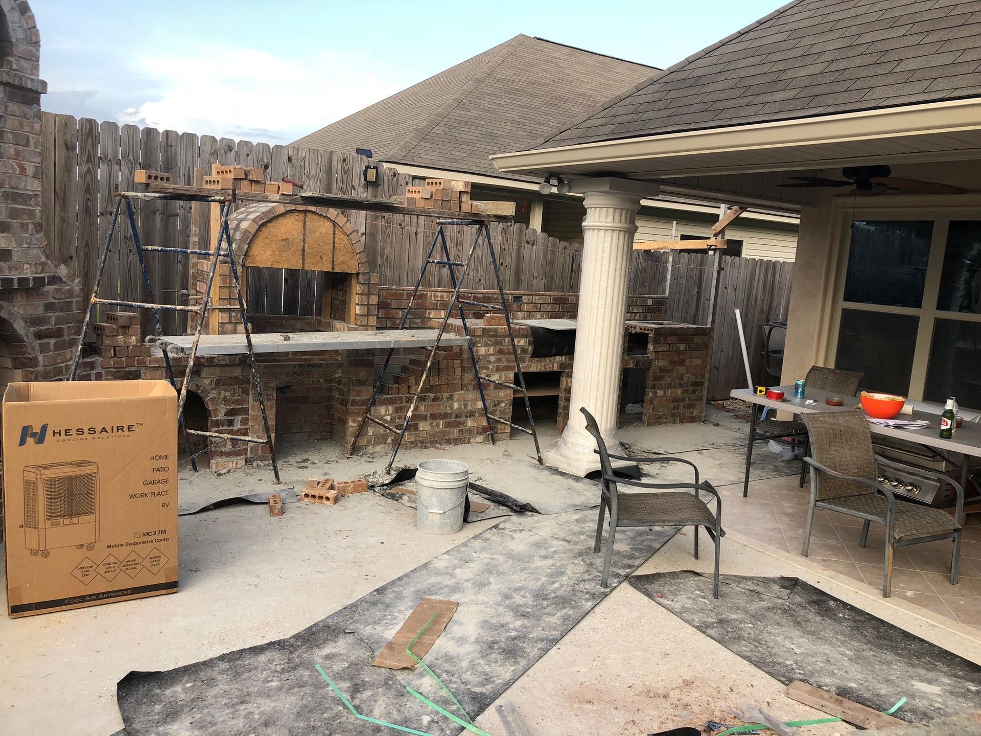 Backyard patio construction with brick pizza oven, brown brick countertop, and wooden fence.