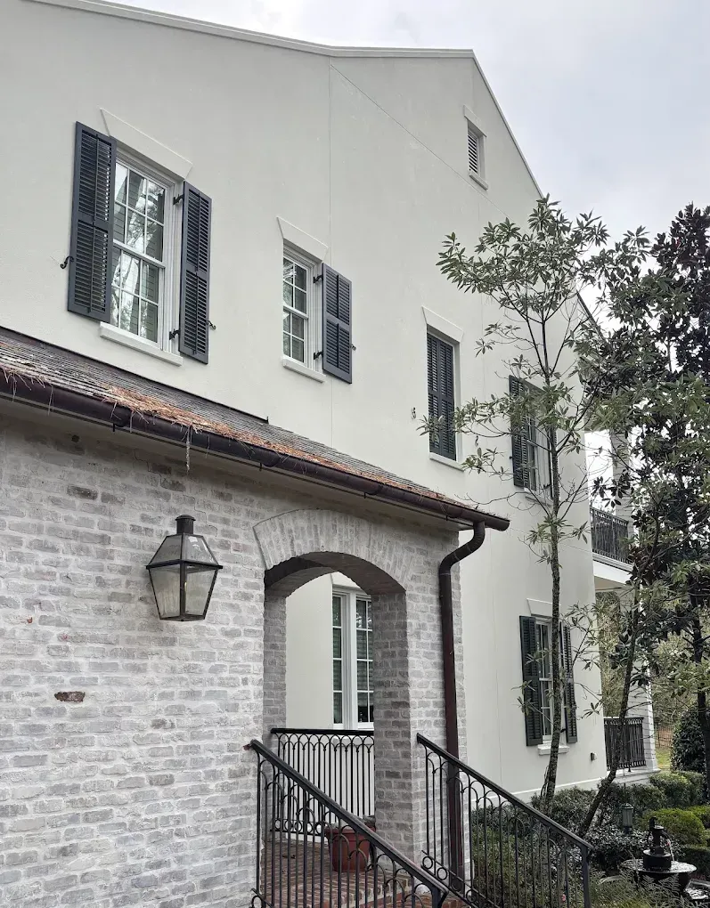 White stucco building with dark shutters and a brick arched entryway.