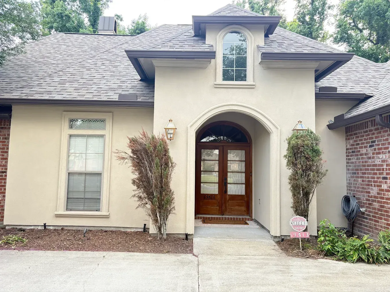 Beige stucco house with brown wooden doors and gray roof. Brick on the right.