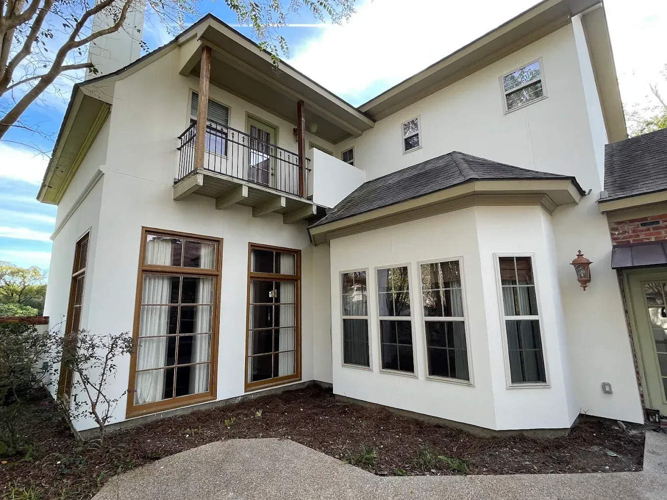 Two-story white house with brown trim and balcony, sunny outdoor view.