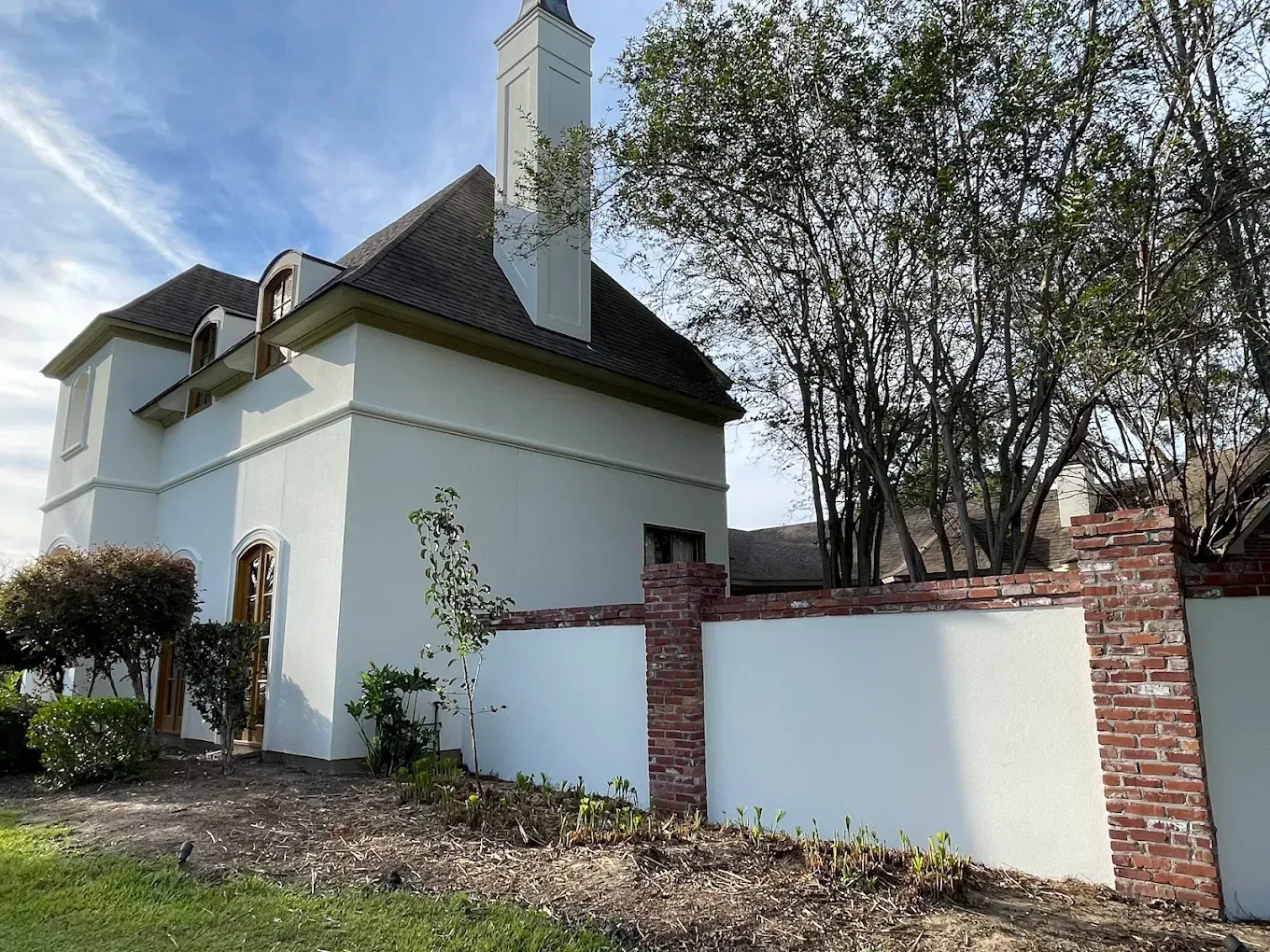 White stucco building with brick accents, chimney, and a small front yard with a partial brick wall.