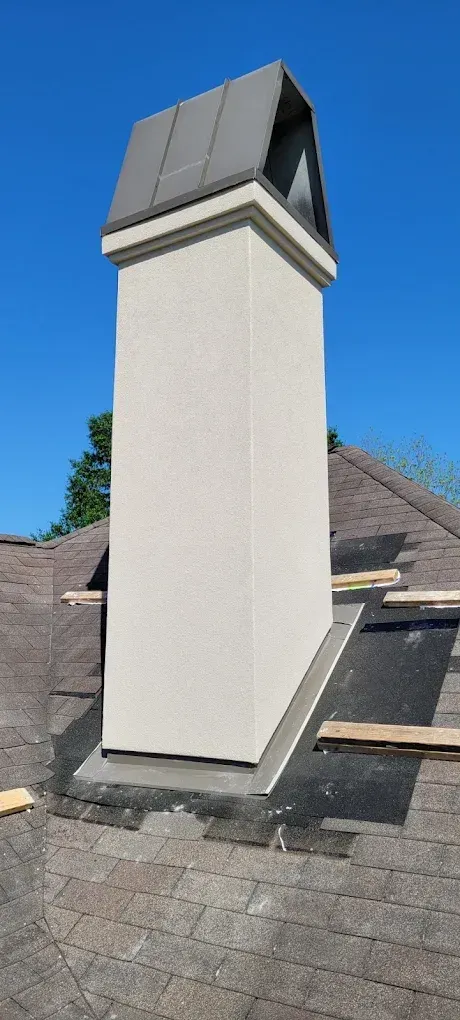 Tall chimney on a roof with a metal cap, against a blue sky.