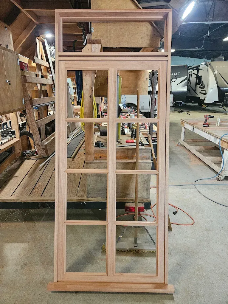 Wooden window frame with multiple panes, constructed in a workshop setting.