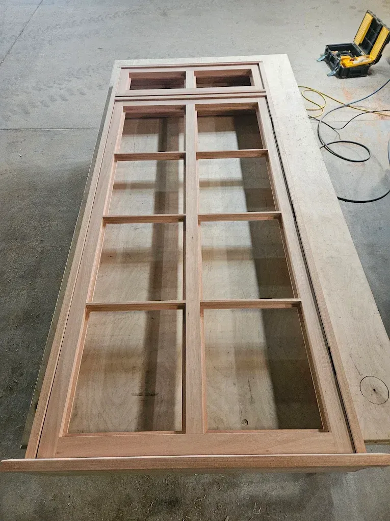 Wooden door with glass panes, constructed on a workbench. A nail gun is in the background.