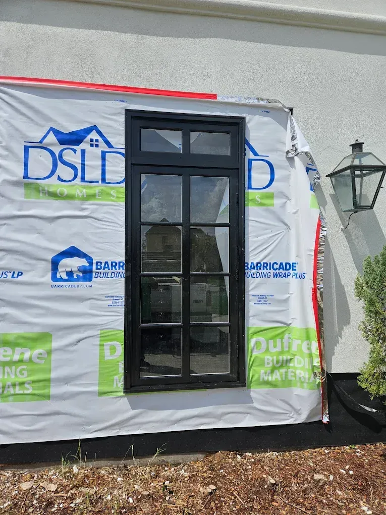 Black-framed window in a white wall with blue-and-white wrap; outdoor setting with a lantern and greenery.