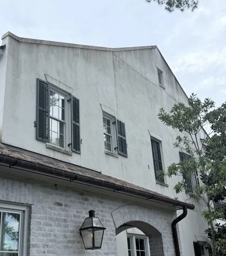 White stucco building with dark shutters and a light brick lower section.
