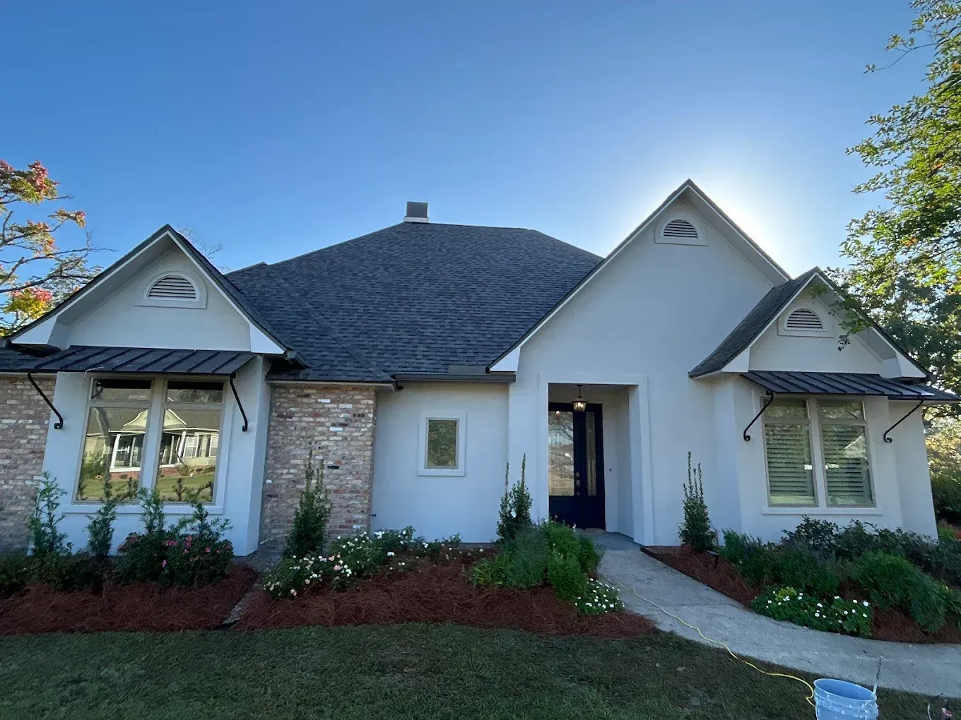White stucco house with dark roof, brick accents, and black front door under a clear sky.