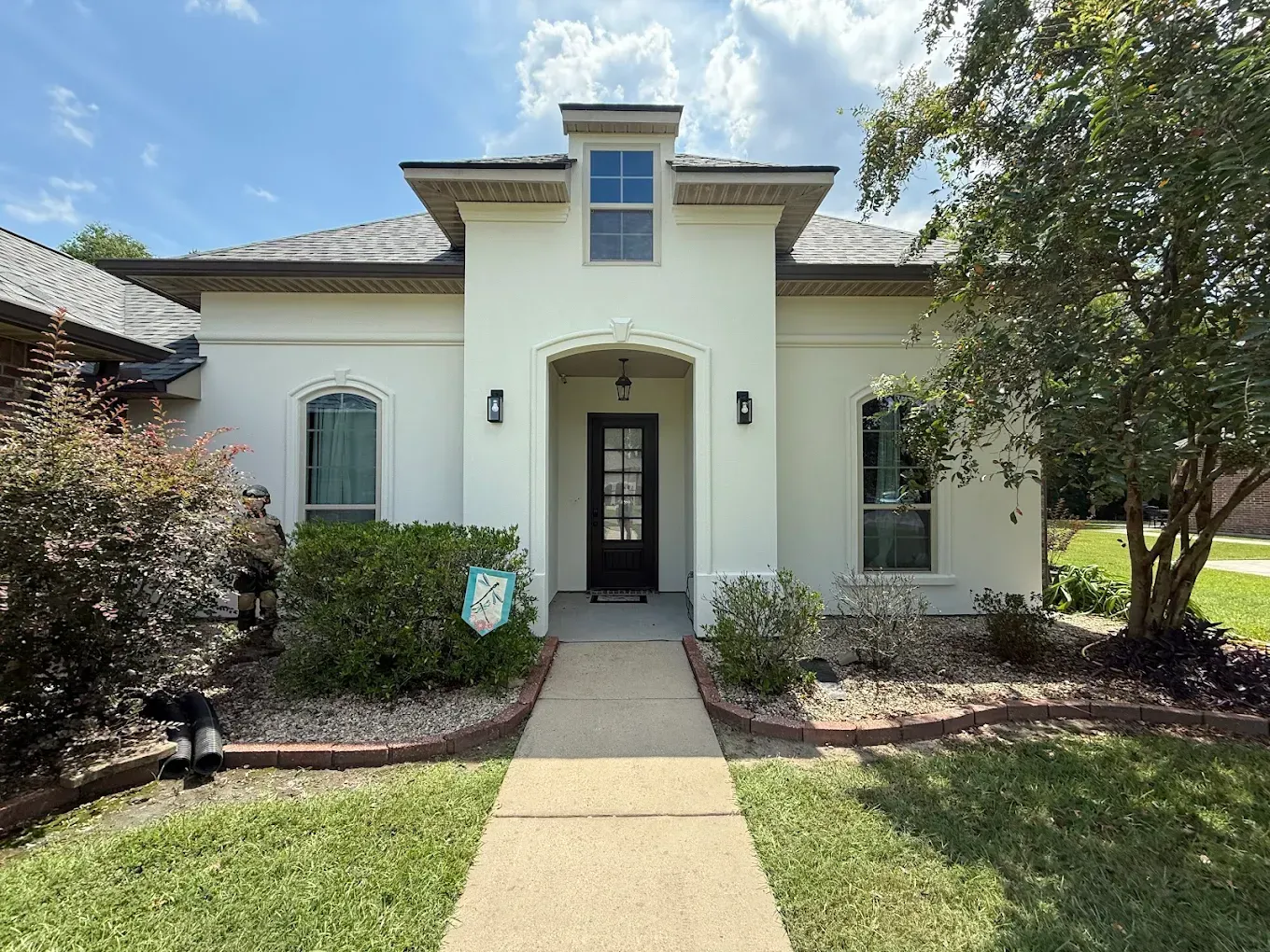 White stucco house with black door, arched windows, and small landscaping.
