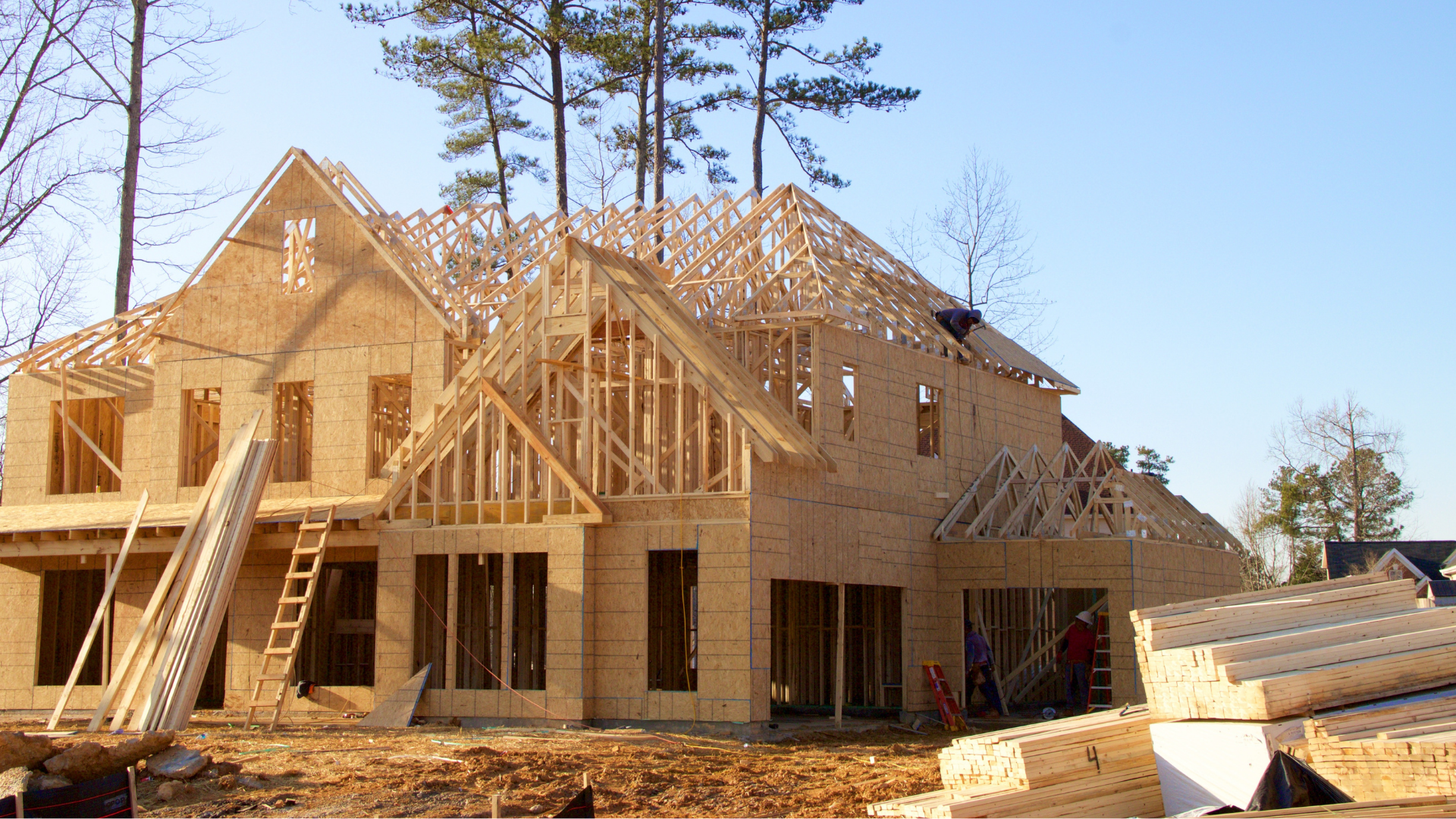 Two-story house under construction; wooden frame, plywood exterior; sunny day.
