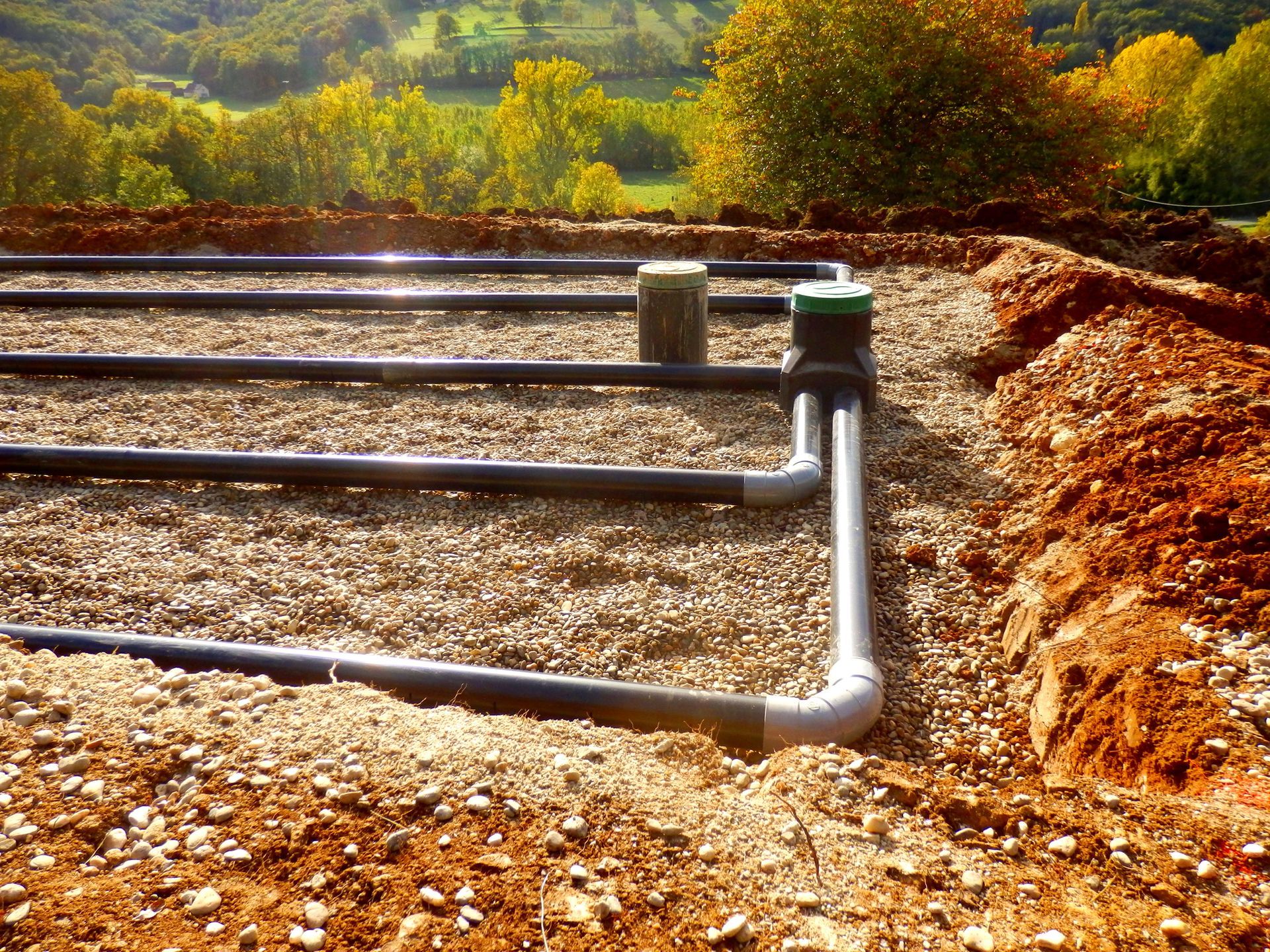 Black irrigation pipes laid across a rocky dirt field with green hills in the background