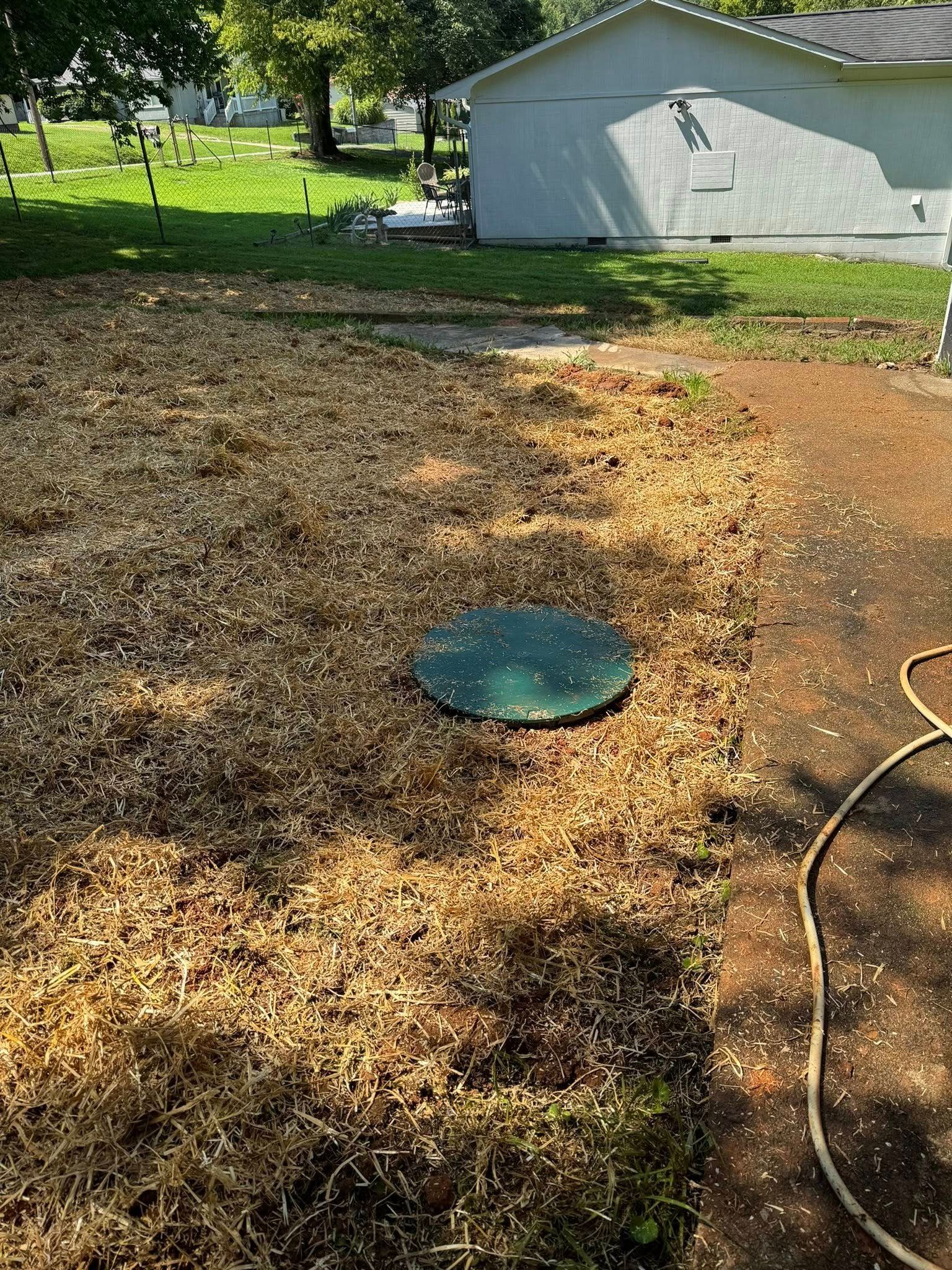 Backyard with gravel and dirt ground, a green septic lid, hose, and a small shed in the background