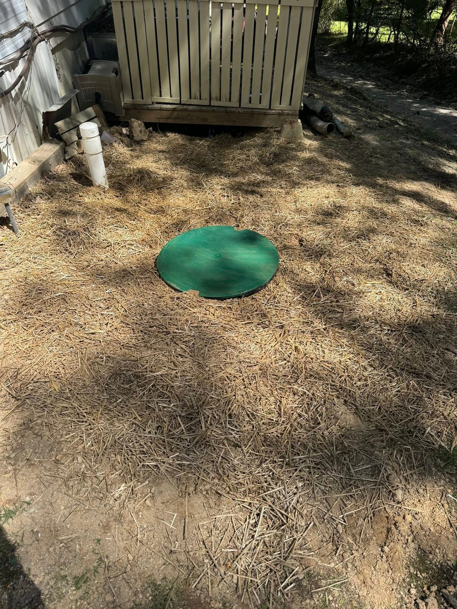 Gravel yard with a green circular cover and a wooden fence in the background