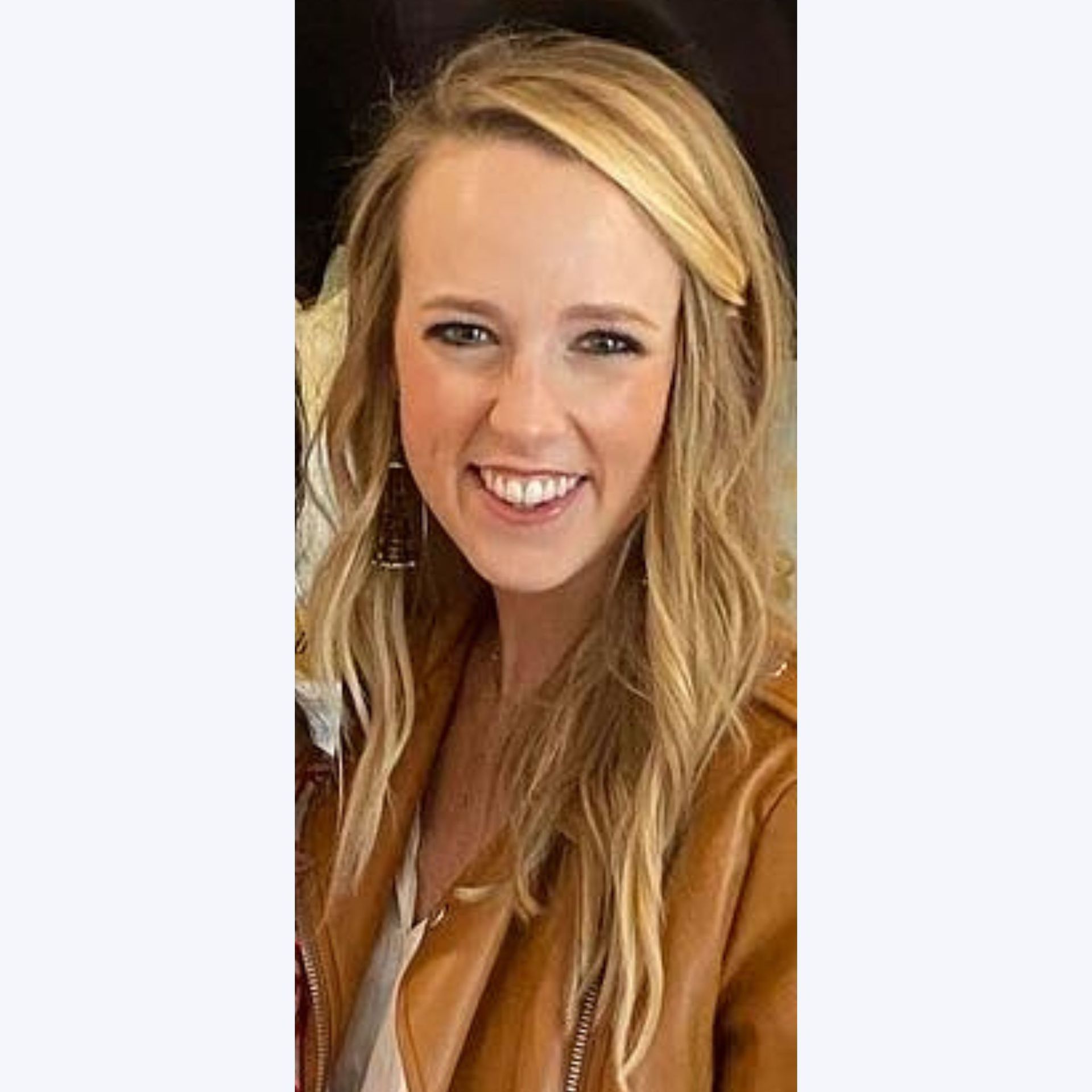 A woman in a brown leather jacket is smiling for the camera.