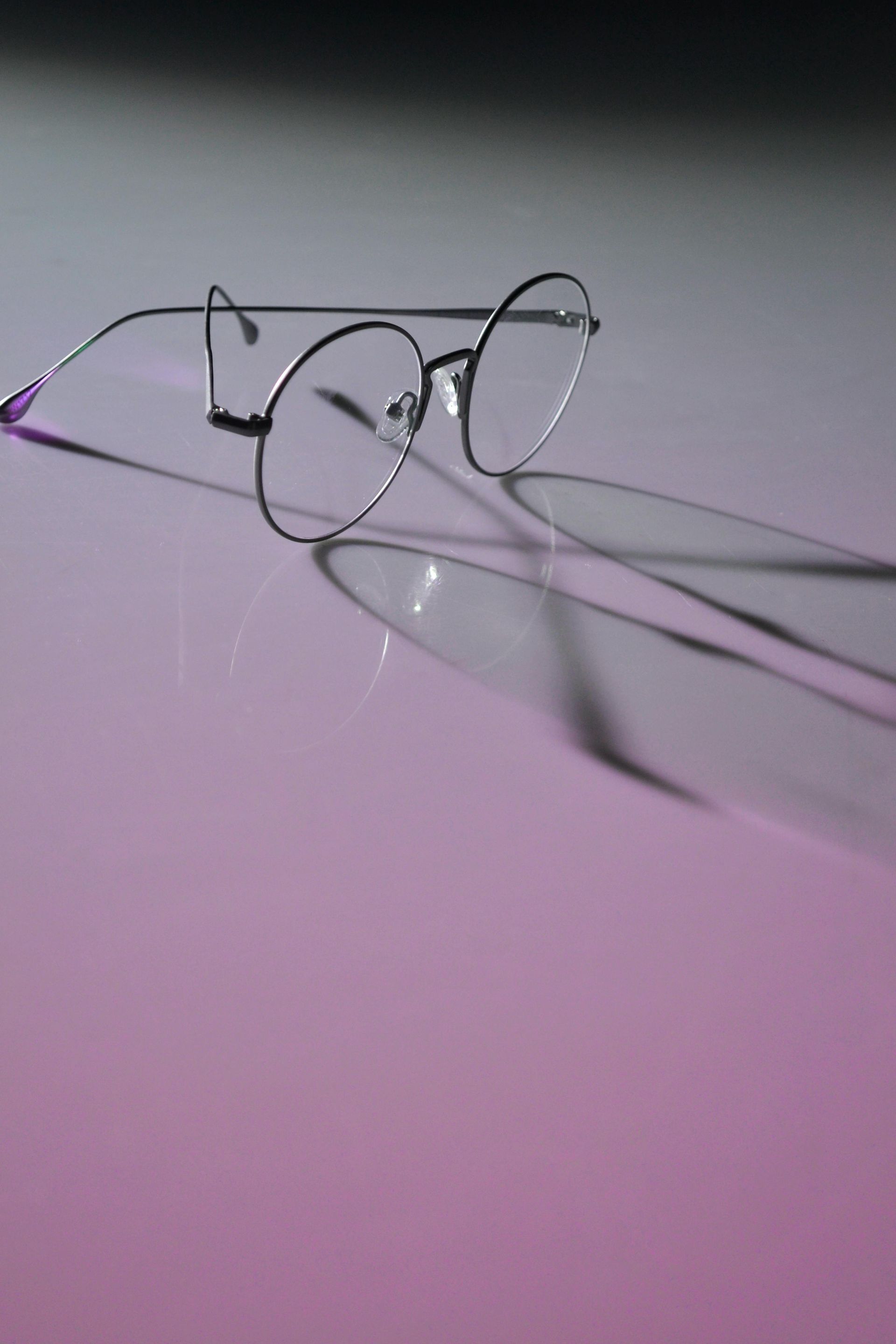 A pair of glasses is sitting on a pink surface.