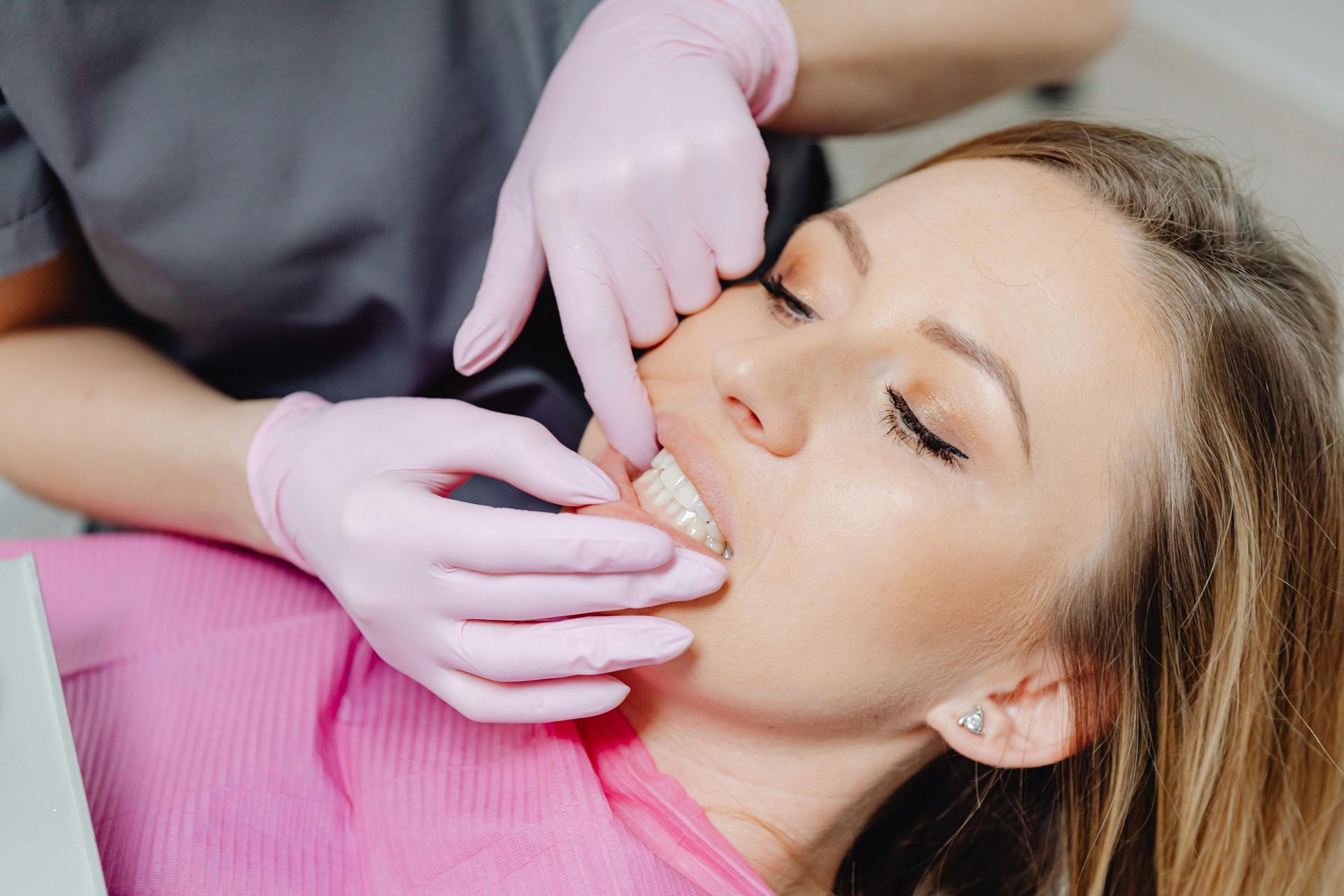 A woman is laying in a dental chair while a dentist examines her teeth.