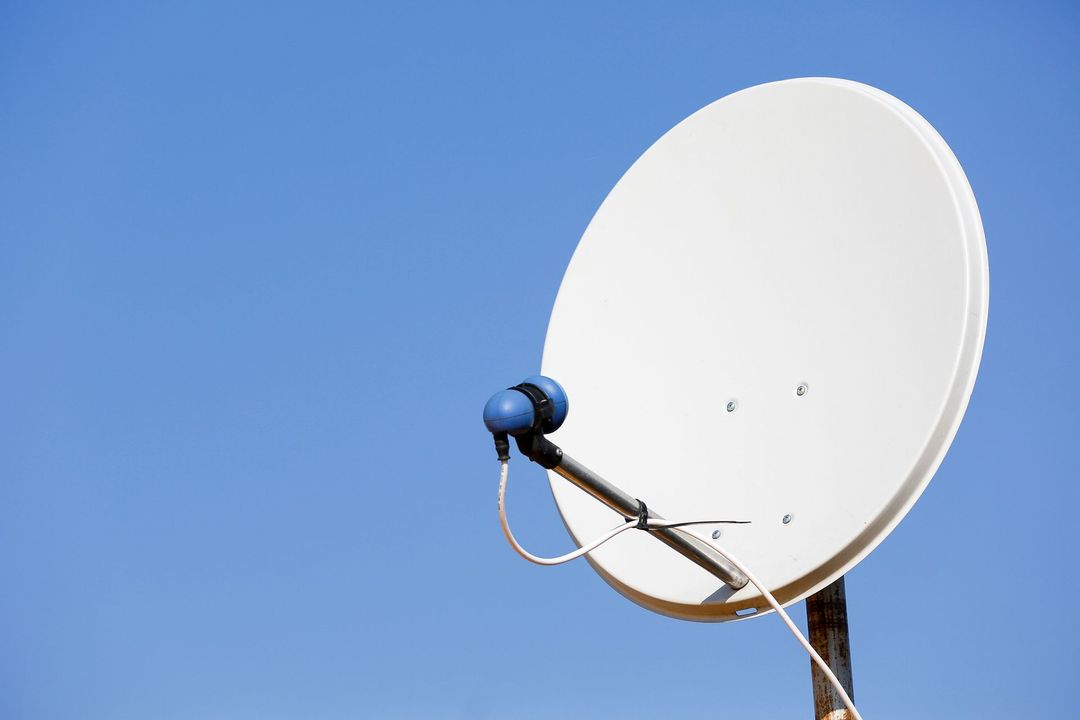 Parabola satellitare bianca contro un cielo azzurro e terso.