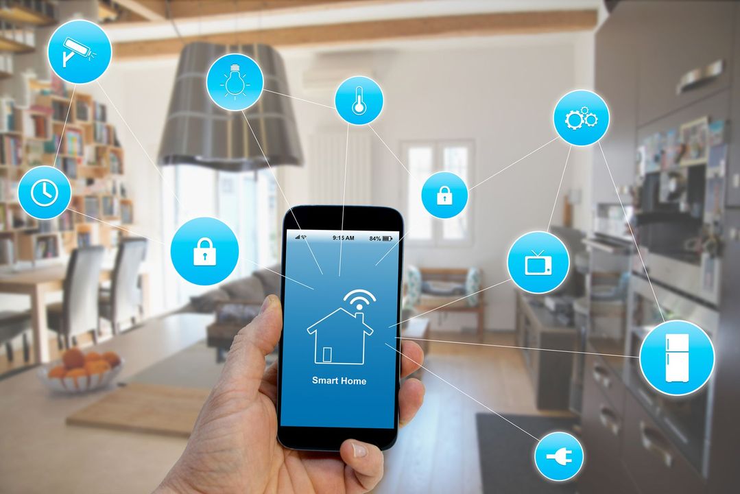 Uno smartphone in mano controlla i dispositivi della smart home in cucina. Le icone blu indicano le varie funzioni.