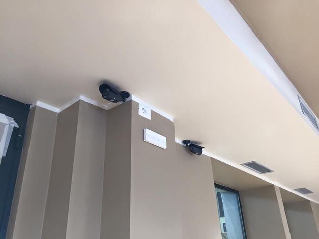Soffitto con altoparlanti neri montati, finiture bianche e pareti beige.