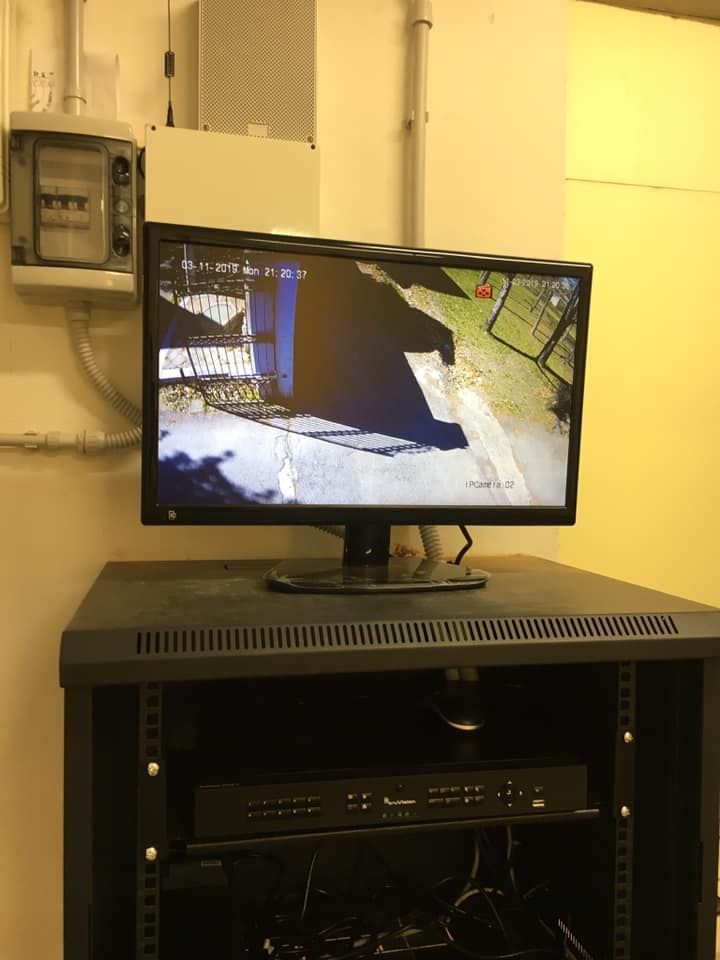 Monitor nero che mostra l'immagine di una telecamera di sorveglianza, montato su un rack insieme ad altre apparecchiature, in una stanza.