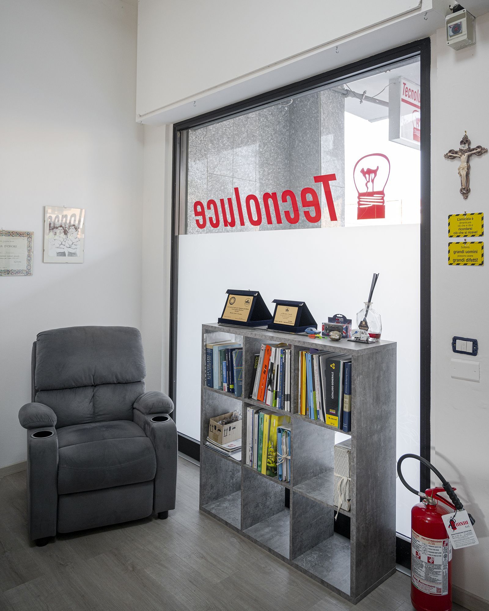 Una poltrona reclinabile grigia e una libreria in un ufficio con una finestra su cui è esposta la scritta