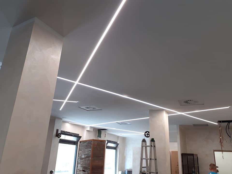Luci LED lineari e luminose si intersecano sul soffitto bianco all'interno di un edificio.