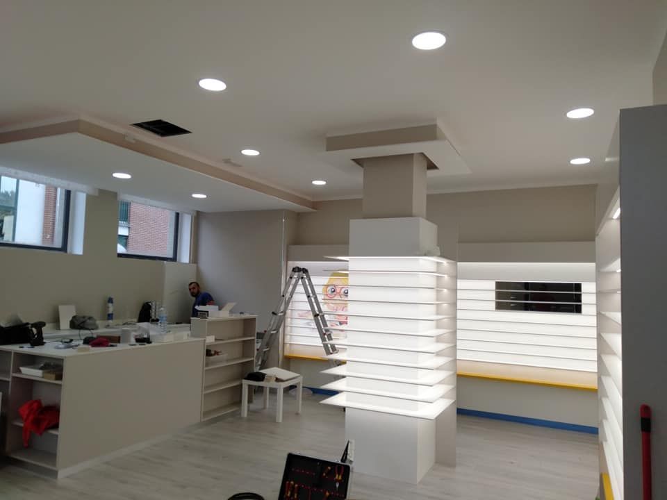 Interno di un negozio con pareti bianche, luci da incasso e una colonna decorativa. Una persona lavora vicino a una scala.