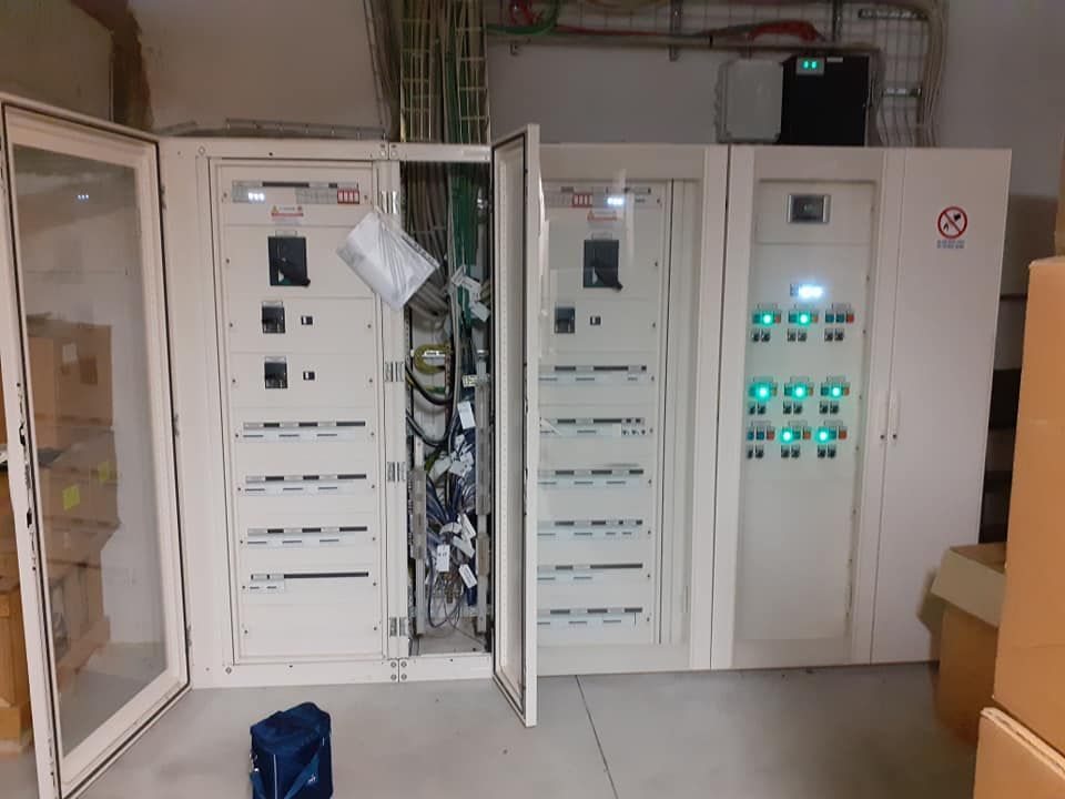 Armadi elettrici bianchi con sportelli aperti, che lasciano intravedere cavi e pannelli, in un ripostiglio.