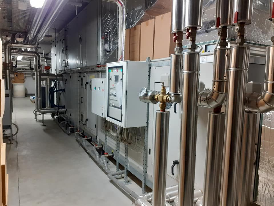 Sistema HVAC in una sala macchine con tubi metallici, canalizzazioni e pannelli di controllo.