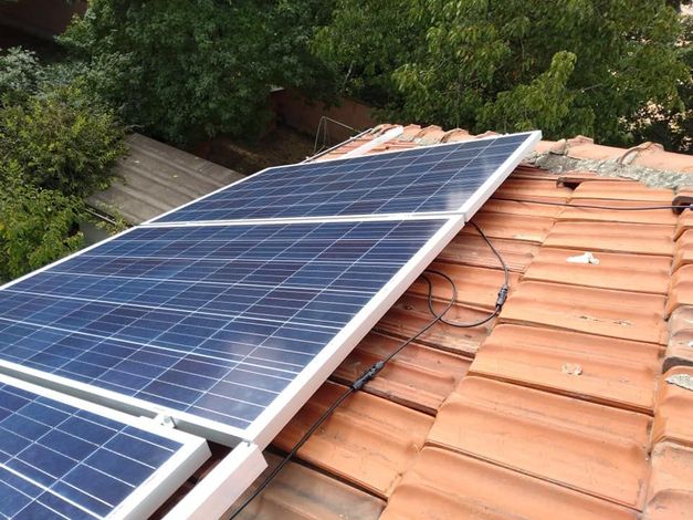 Pannelli solari installati su un tetto di tegole rosse, cavi visibili, circondato da alberi.