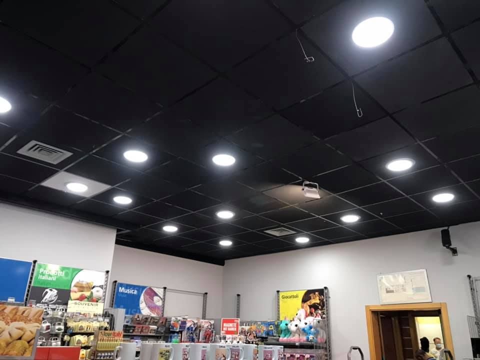 Soffitto piastrellato nero con luci circolari luminose in un negozio. Espositori e pareti bianche sottostanti.