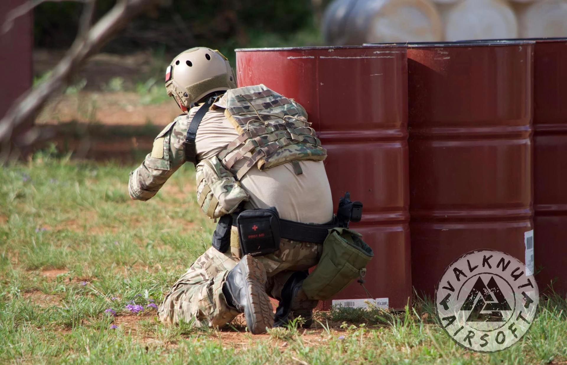 A soldier is kneeling down in front of a red barrel