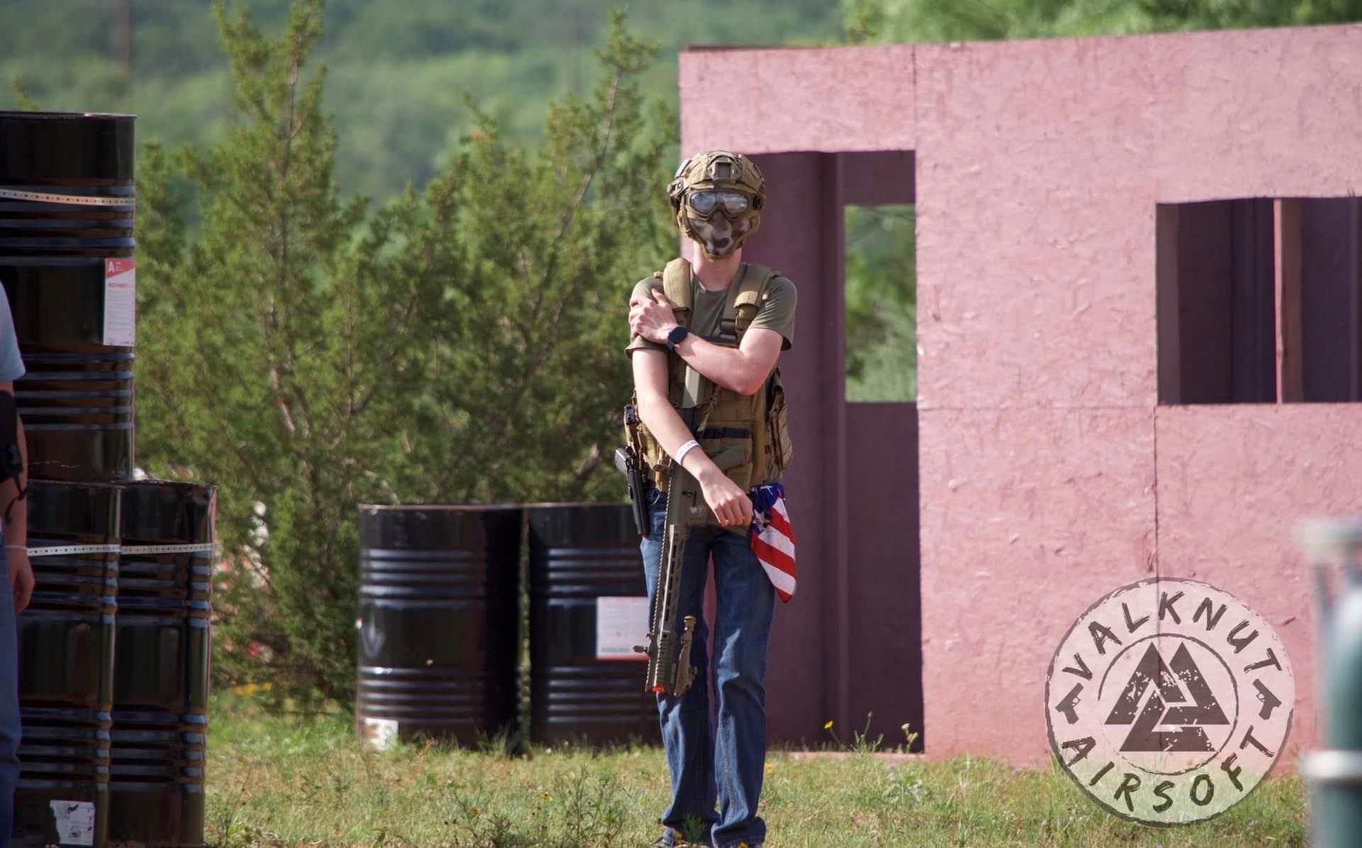 A man wearing a helmet and holding an american flag is standing in a field