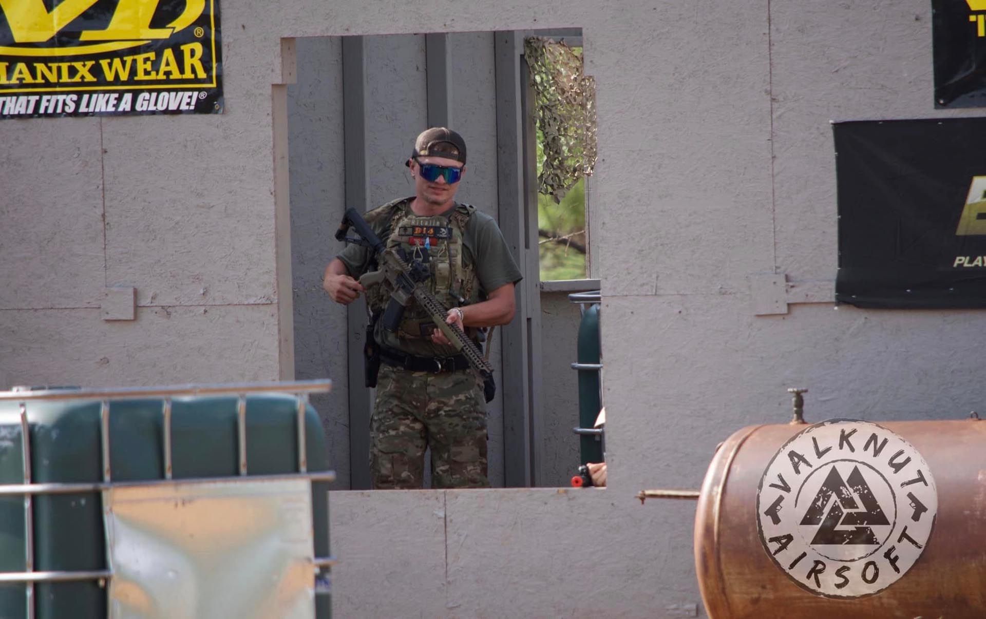 A man is standing in front of a wall with a sign that says walknut airsoft