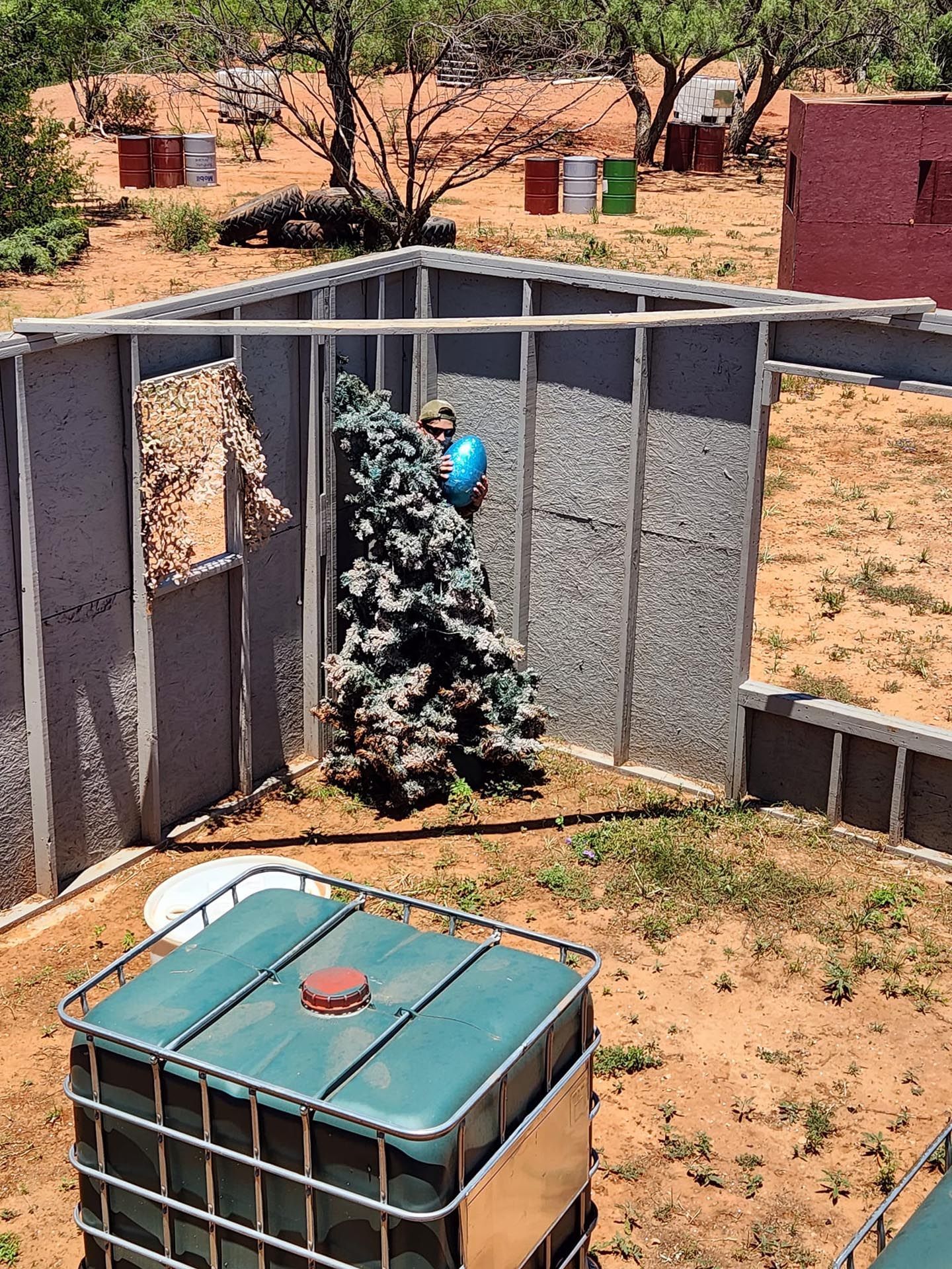 A container with a green lid is sitting in the dirt in front of a fence