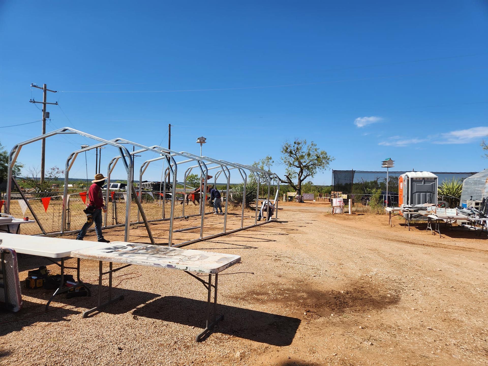 A group of people are working on a greenhouse in a dirt field