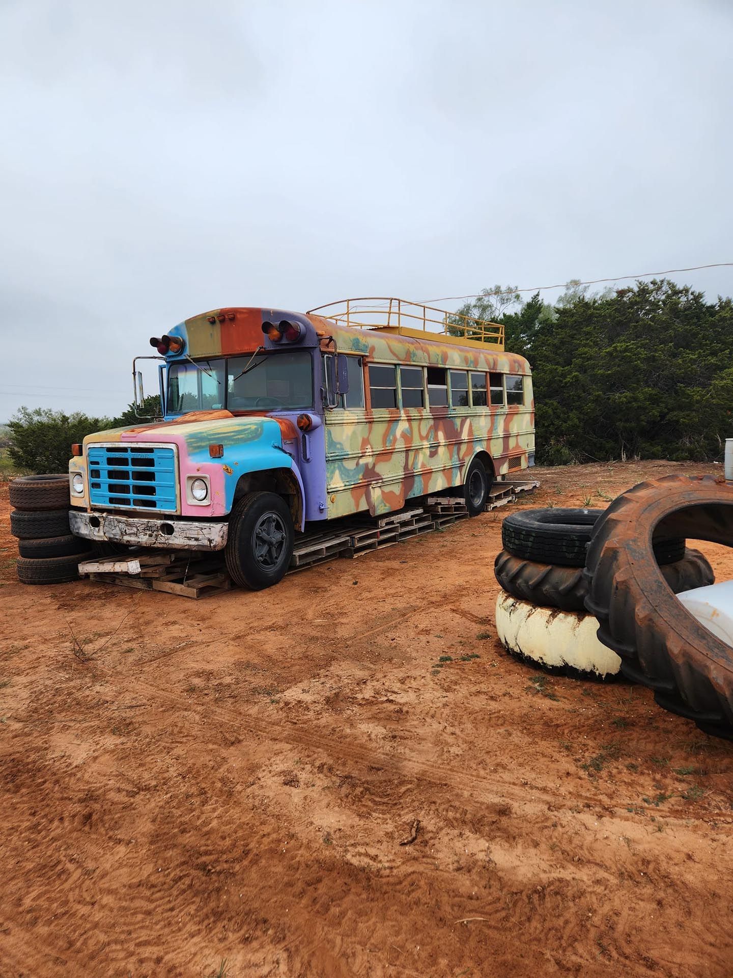 A colorful school bus is parked in a dirt field next to a pile of tires