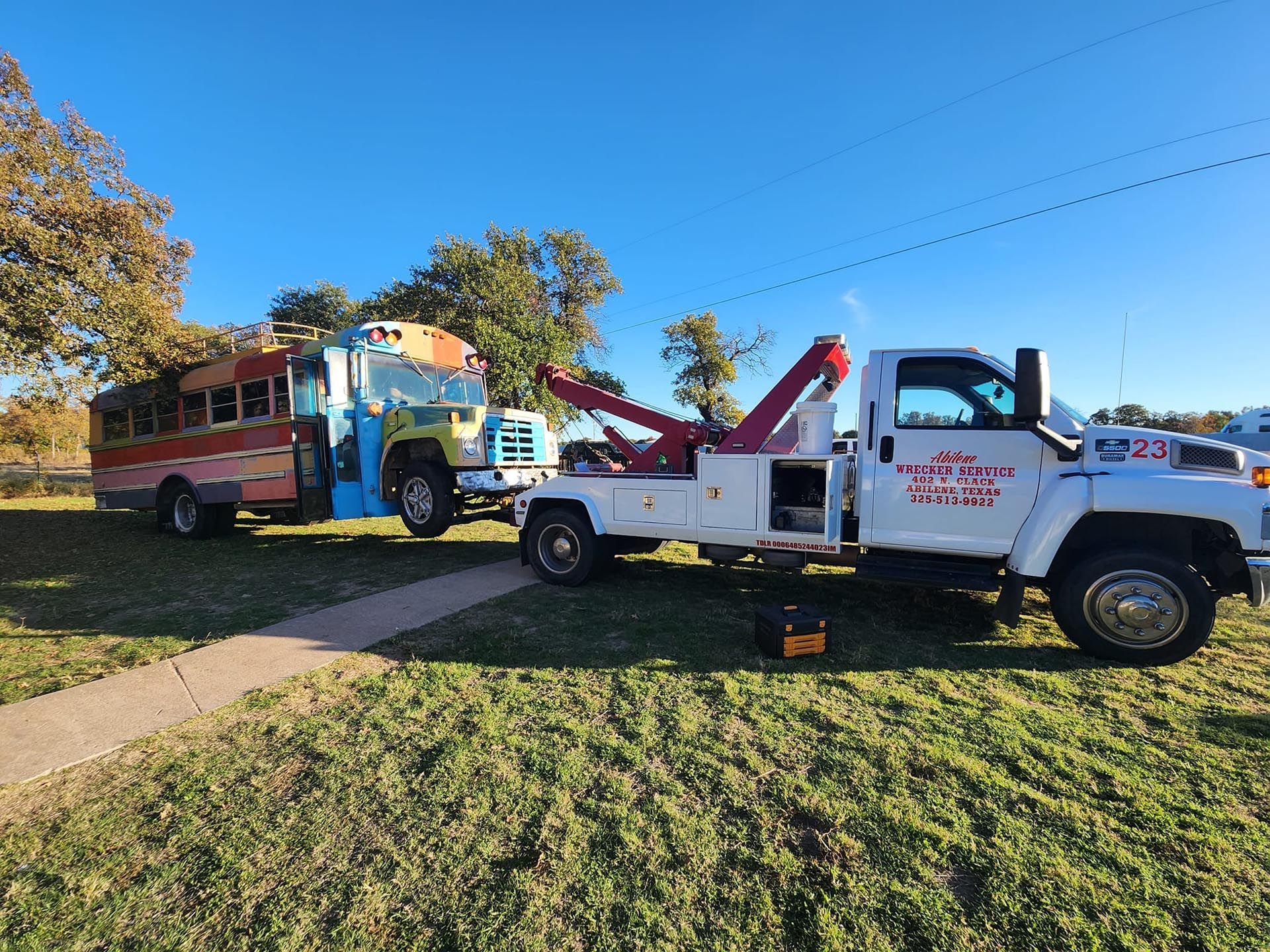 A tow truck is towing a school bus in a grassy field