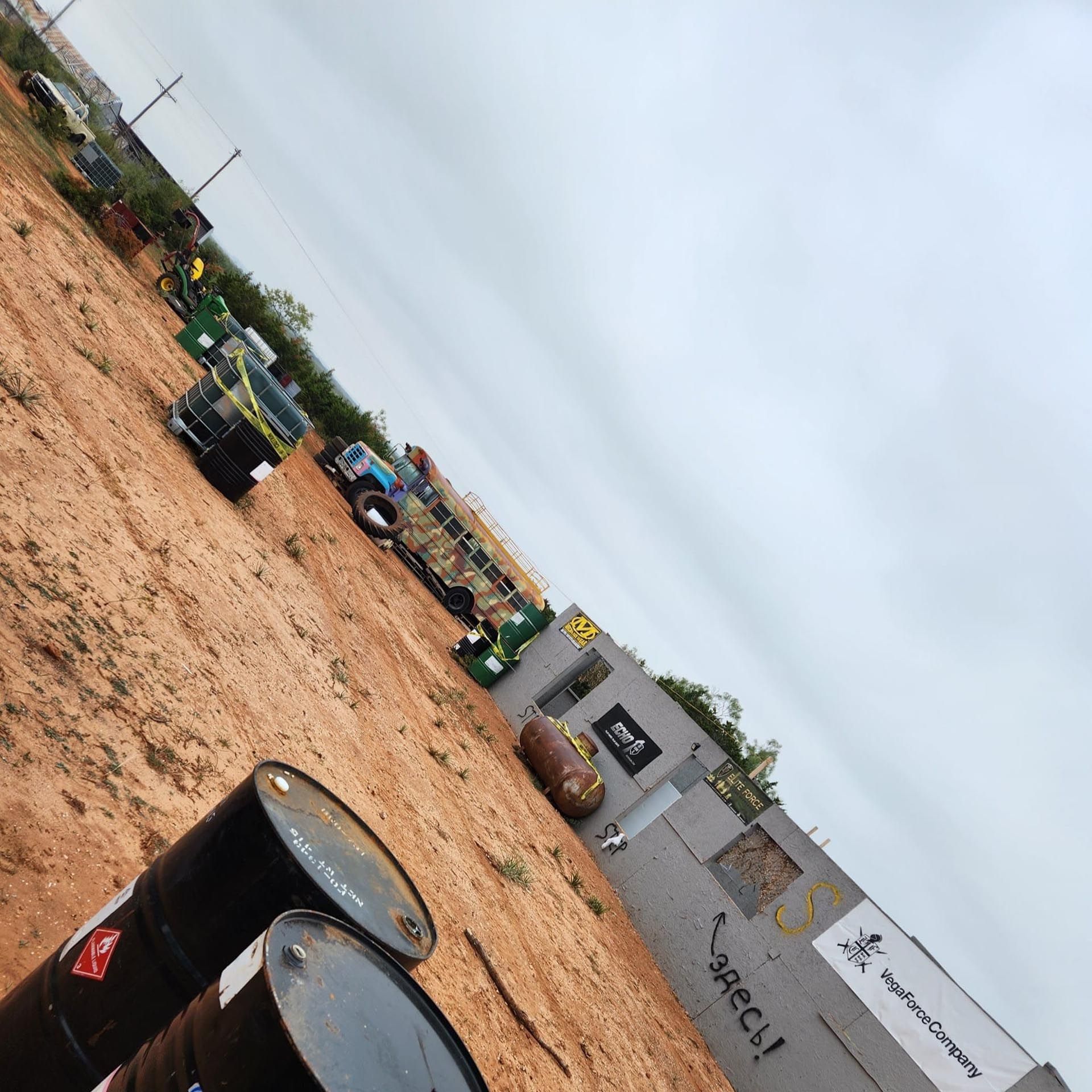 Several barrels are lined up in a dirt field and one of them has the word spec written on it
