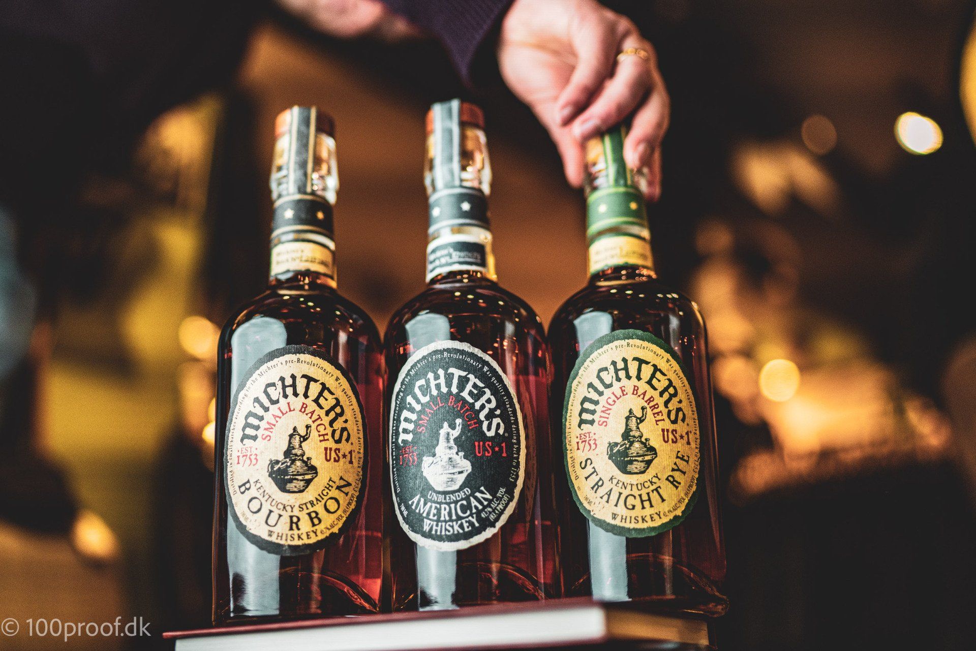 En person holder tre flasker bourbon på en bakke.